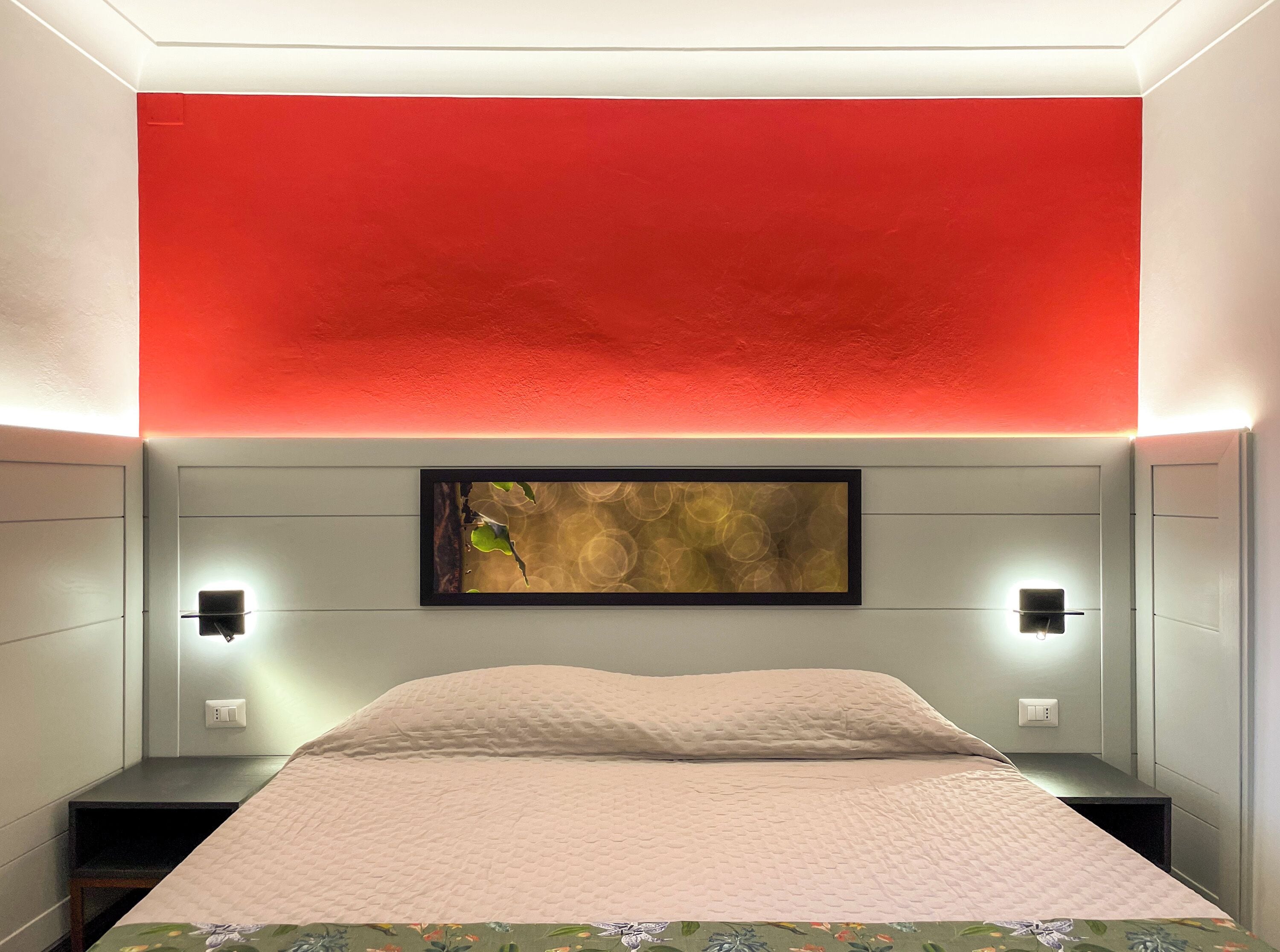 A bedroom with a bed, a red accent wall, a framed artwork, and bedside lamps.