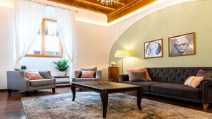Una sala de estar con un sofá, un sillón, una mesa de centro y una lámpara. Hay dos cuadros enmarcados en la pared.