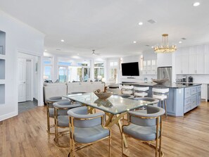 Une cuisine moderne avec des meubles blancs, un grand îlot central et un coin repas comprenant une table en verre et quatre chaises.