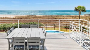 Un terrazzo in legno con tavolo e sedie, affacciato su una spiaggia e una piscina.
