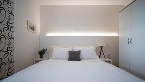Une chambre à coucher bien rangée, avec un lit, une table de chevet, une lampe et une armoire.