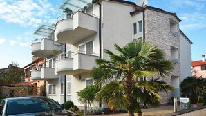 Un immeuble résidentiel à plusieurs étages, doté de balcons, d’une façade en pierre et d’un palmier au premier plan.