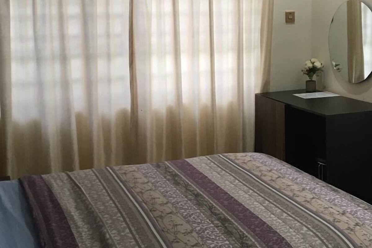 A bedroom with a bed, a vanity with a mirror, and an air conditioner on the wall.