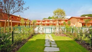 A courtyard with a stone pathway leading to a gated entrance, surrounded by greenery and a row of orange buildings with multiple balconies. - Seaside Apartment in Santa Cruz Tenerife (Lignano Sabbiadoro)