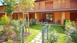A two-story building with a balcony, a small garden with a lawn and a stone pathway, and outdoor seating with chairs. - Seaside Apartment in Santa Cruz Tenerife (Lignano Sabbiadoro)