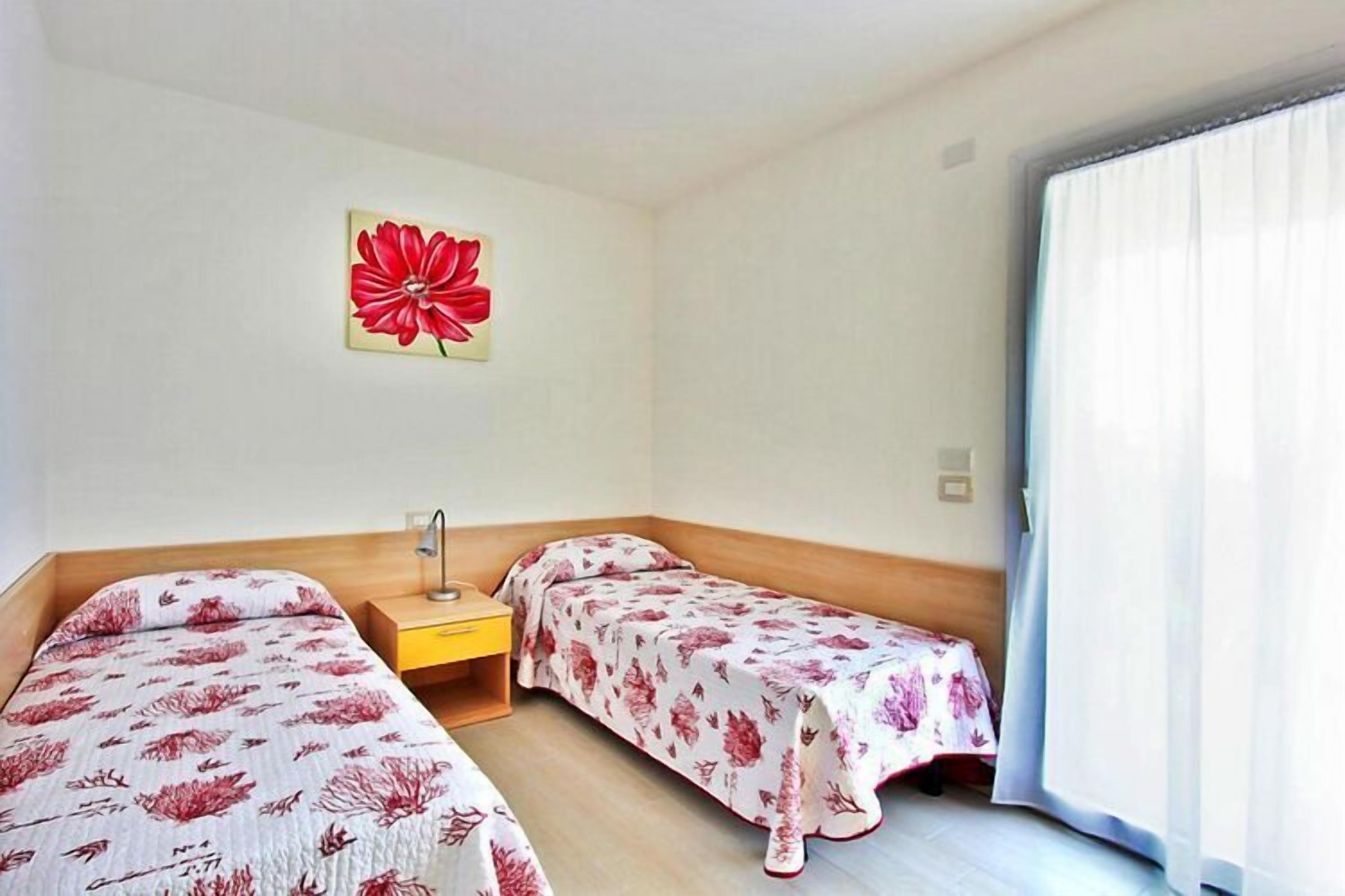 Una habitación con dos camas, una mesita y un ventanal con cortinas.