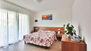 A hotel room with a bed, a nightstand, a wall-mounted painting, and a potted plant. - Apartment near the beach in Lignano (Lignano)