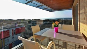 A balcony with a glass table and chairs, a potted plant, and a view of the cityscape. - Apartment near the beach in Lignano (Lignano)