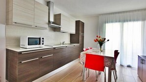A modern kitchen with a microwave, dark wooden cabinets, and a dining area with a red table and chairs. - Apartment near the beach in Lignano (Lignano)