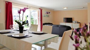 Zona pranzo con tavolo imbandito per due, divano e televisione sullo sfondo.