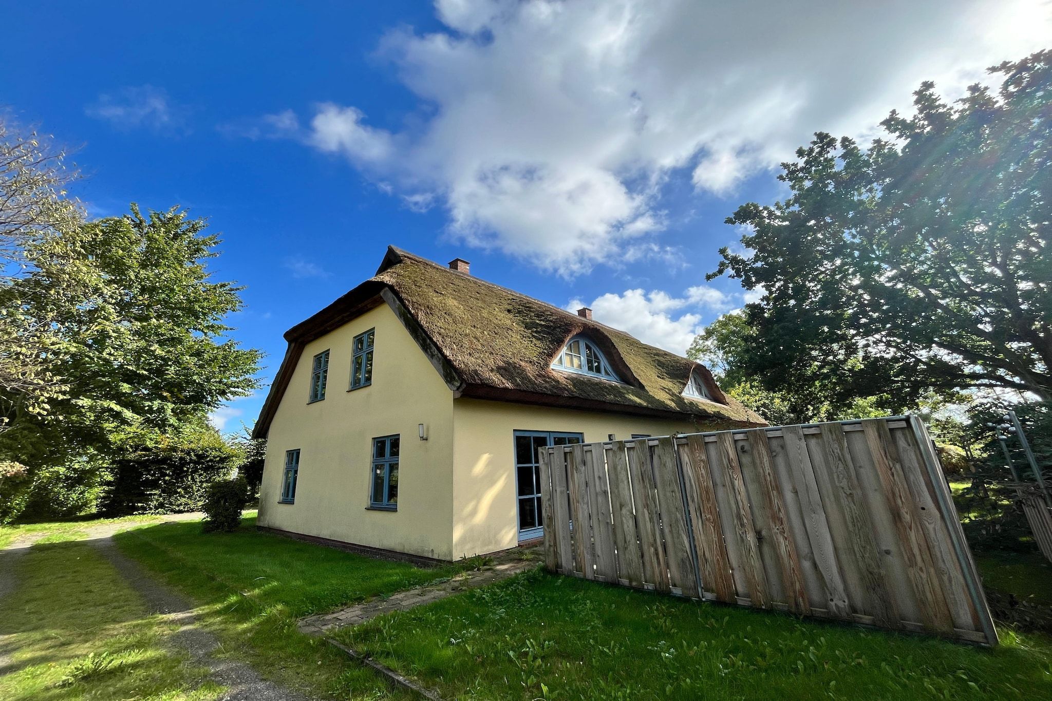 A single-story house with a thatched roof, a wooden fence, and a clear sky.