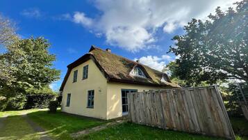 A single-story house with a thatched roof, a wooden fence, and a clear sky.