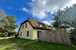 Une maison de plain-pied avec un toit de chaume, une clôture en bois et un ciel dégagé.