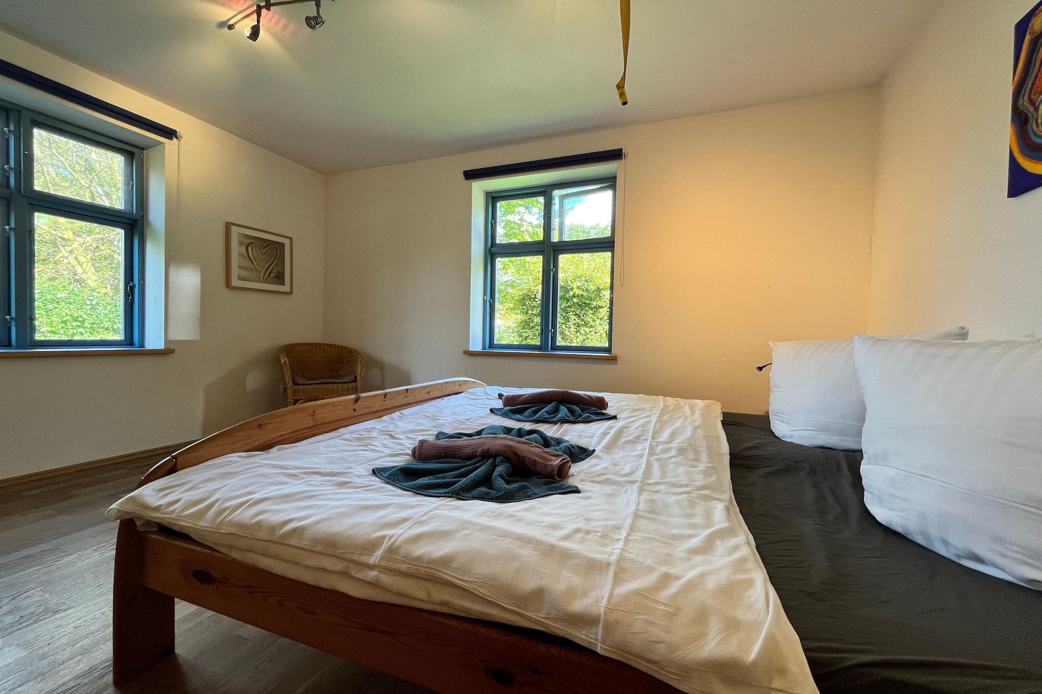 A bedroom with a wooden bed, two windows, a chair, and a wall-mounted picture.