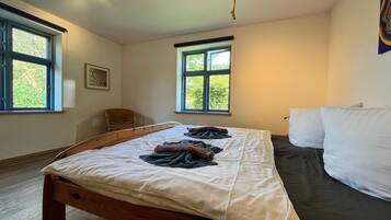 A bedroom with a wooden bed, two windows, a chair, and a wall-mounted picture.
