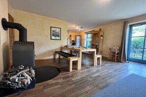 Un salon chaleureux avec une cheminée, un coin repas et une vue dégagée sur l’extérieur grâce à une grande fenêtre.
