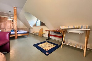Ein Zimmer mit schrägem Dach, einem Bett, einem Schreibtisch, einem Stuhl und einem kleinen Tisch.