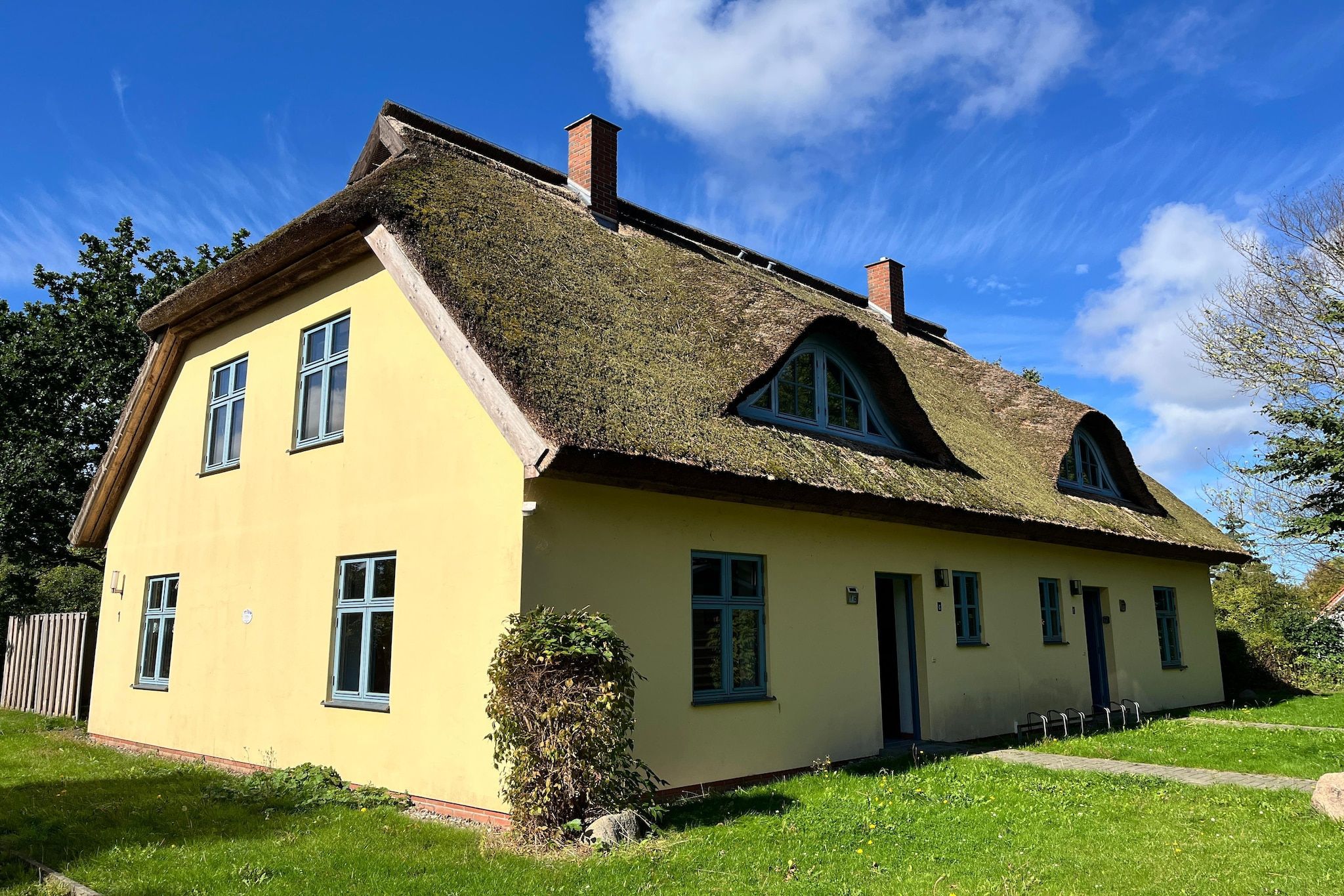 Ein zweistöckiges Haus mit Strohdach, einer gelben Fassade und zahlreichen Fenstern.
