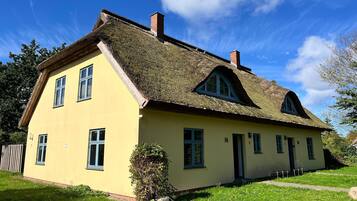 A two-story house with a thatched roof, a yellow facade, and multiple windows.