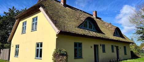 Ein zweistöckiges Haus mit Strohdach, einer gelben Fassade und zahlreichen Fenstern.