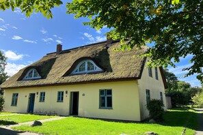 Une maison traditionnelle avec un toit de chaume, un petit porche et une pelouse bien entretenue.