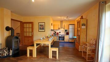 A cozy living space with a wooden table, benches, a kitchen area with appliances, and a fireplace.