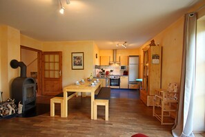 Un espace de vie chaleureux avec une table en bois, des bancs, un coin cuisine équipé d’appareils électroménagers et une cheminée.