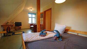 A bedroom with a bed, a desk, a chair, a television, and a window.