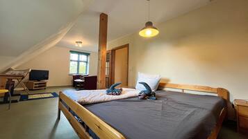Een slaapkamer met een schuine kap, een bed met kussens, een bureau met een computer en een raam.