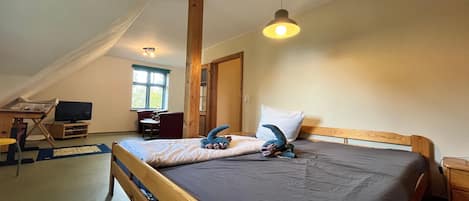 Un dormitorio con techo inclinado, cama con almohadas, escritorio con computadora y ventana.
