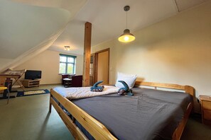 A bedroom with a sloped ceiling, a bed with pillows, a desk with a computer, and a window.