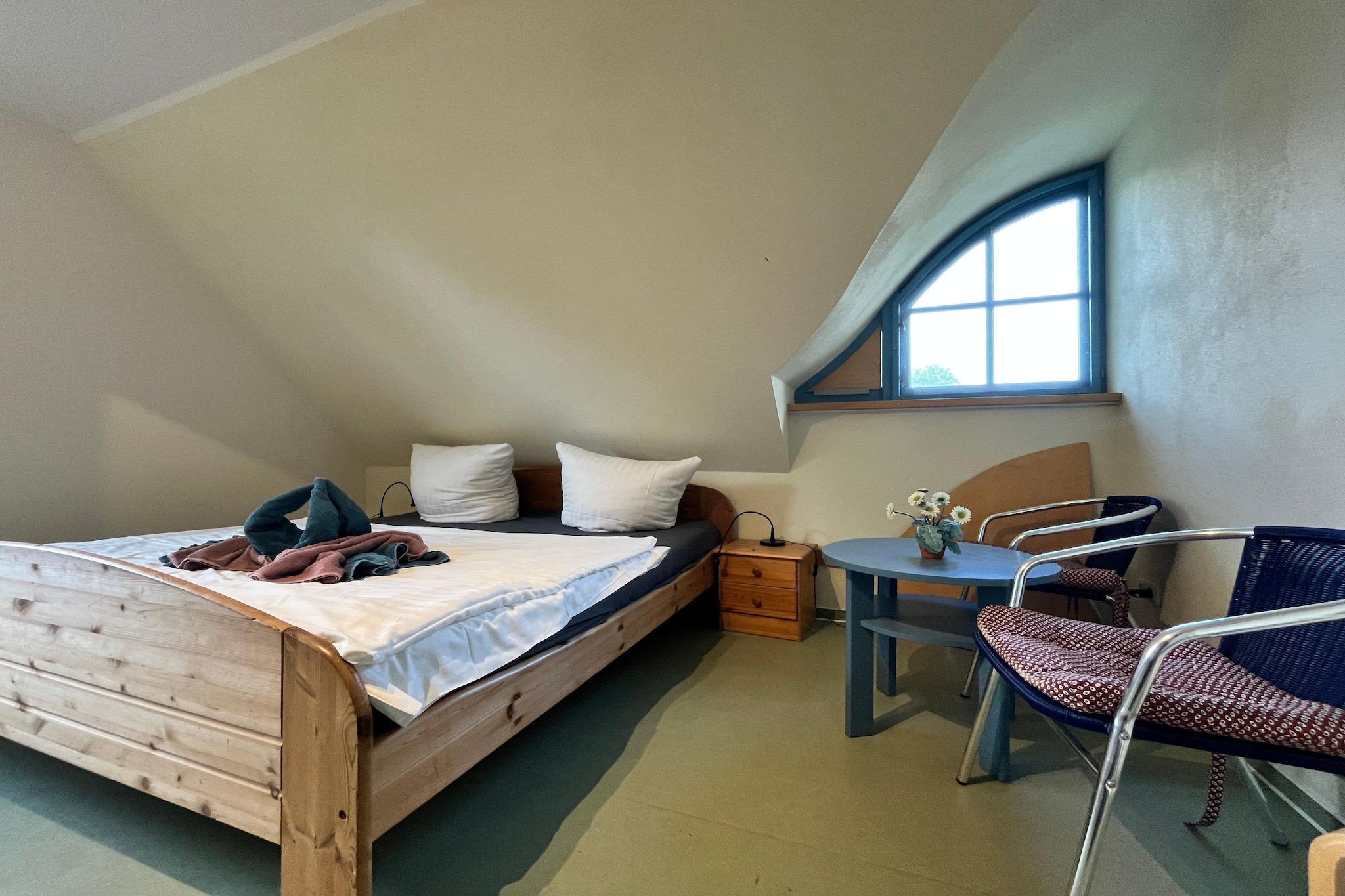 A bedroom with a sloped ceiling, a bed, a bedside table, a chair, and a window.