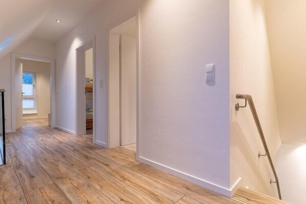 A hallway with wooden flooring, white walls, and a staircase with a handrail.