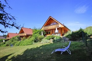 A wooden lodge with a sloped roof, a balcony, and a well-maintained garden.