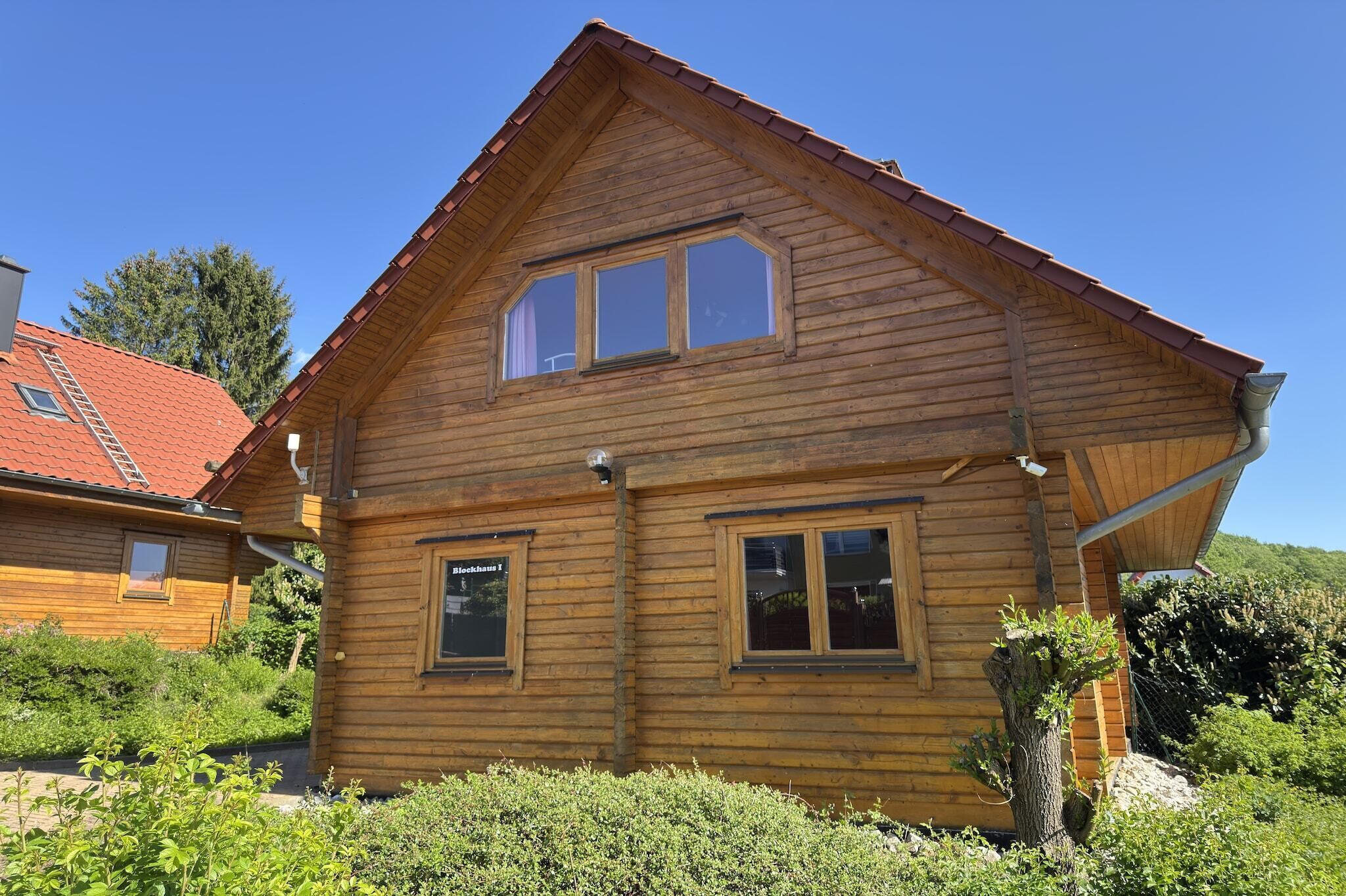 Una casa de madera con techo inclinado, dos ventanas y una chimenea visible.