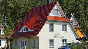 A two-story building with a red-tiled roof, a white facade, and a sign that reads "Machtigall". - Ferienhaus Nachtigall, Glowe (Glowe)