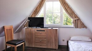 A bedroom with a sloped ceiling, a wooden desk with a TV, a chair, a bed, and a window with curtains. - Ferienhaus Nachtigall, Glowe (Glowe)