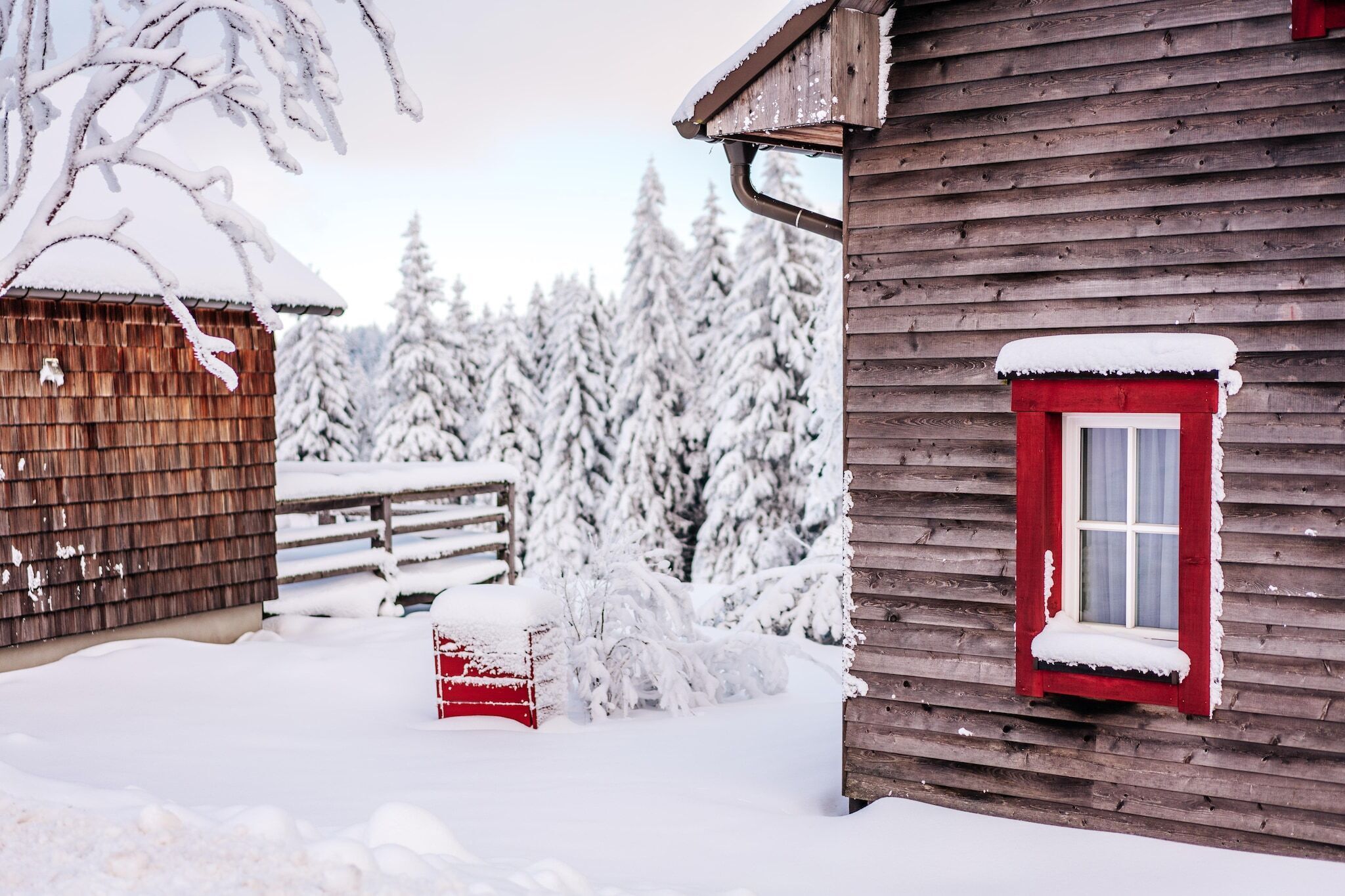 A wooden cabin with a red window and snow-covered surroundings.