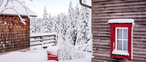 A wooden cabin with a red window and snow-covered surroundings.