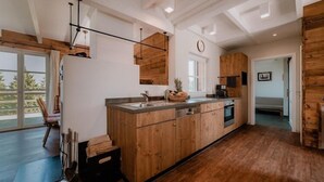 A modern kitchen with wooden cabinets, a central island, and a large window. - Ferienhäuser im Torfhaus Harzresort, Torfhaus (Torfhaus)