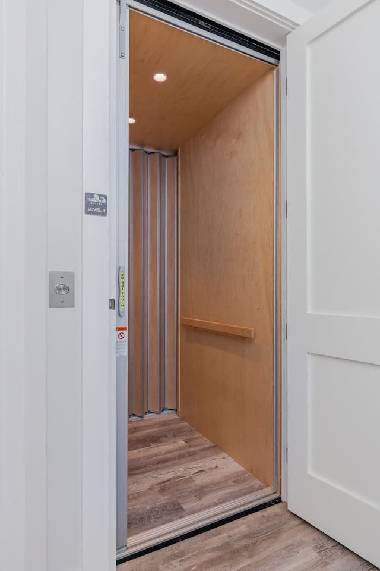 Un ascenseur étroit avec un intérieur en bois, un panneau indiquant clairement la sortie de secours et une main courante métallique.