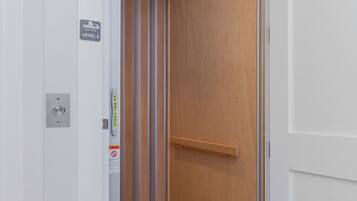 Un ascenseur étroit avec un intérieur en bois, un panneau indiquant clairement la sortie de secours et une main courante métallique.