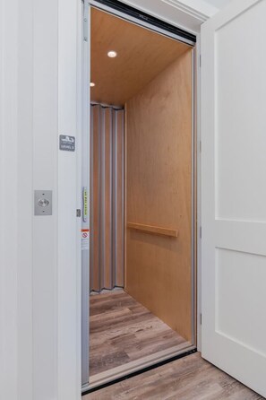 A narrow elevator with a wooden interior, a visible emergency exit sign, and a metallic handrail. - Manatee Suite 2 / Funky Fish House at Cape Harbour (Cape Coral)