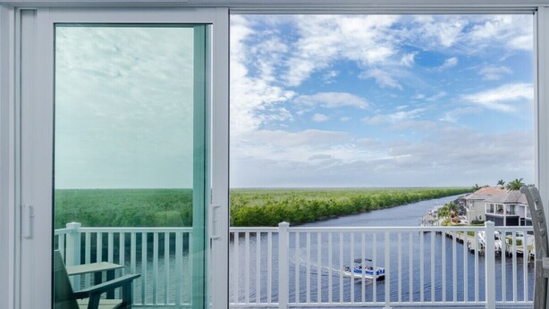 Un balcón con puerta de cristal, una mesa y vista a un canal con barcos y casas.