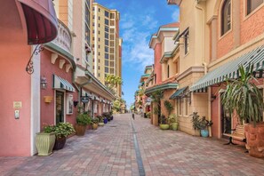 A narrow street lined with buildings, some with balconies and awnings, and potted plants along the sidewalk.