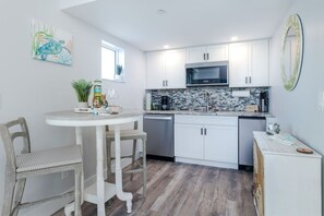 A modern kitchen with white cabinetry, a stainless steel microwave, and a tiled backsplash.