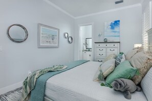 A bedroom with a bed, a dresser, a mirror, and wall art.
