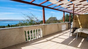 Un espace extérieur abrité, doté d’une table et de chaises, offrant une vue sur la mer et bordé d’un mur en pierre.