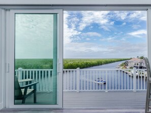 Un balcon avec une porte vitrée, une table et une vue sur un cours d’eau où l’on peut voir des bateaux et des maisons.