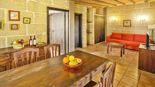 A dining area with a wooden table, chairs, and a fruit bowl. There is a red sofa and a lamp in the living area. - Romantic Getaway in Malpais de Candelaria (Malpais de Candelaria)